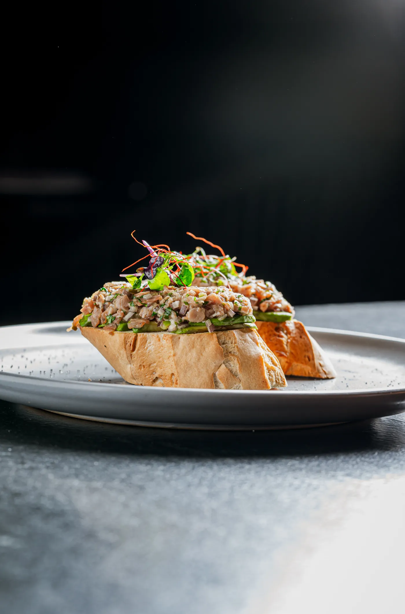 Tostada de pan con tartar y brotes sobre fondo oscuro