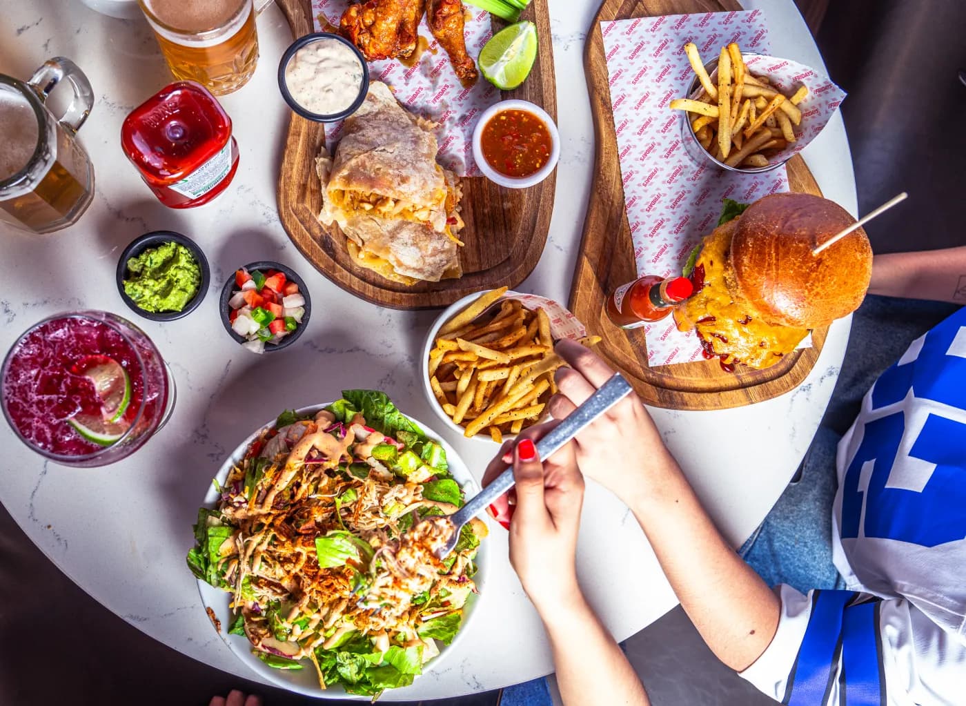 Mesa vista desde arriba con platillos para compartir, papas y bebidas