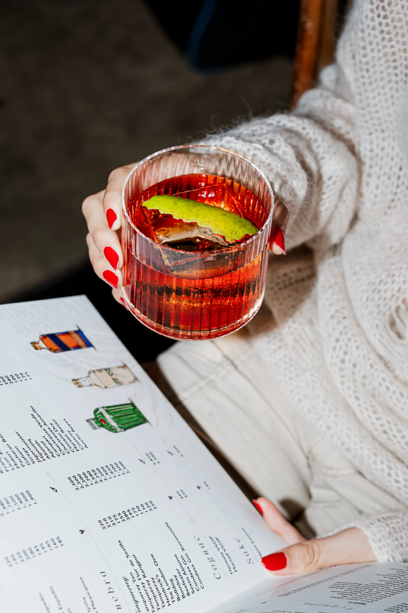 Mano que sostiene un coctel rojo con hielo sobre una carta de bebidas