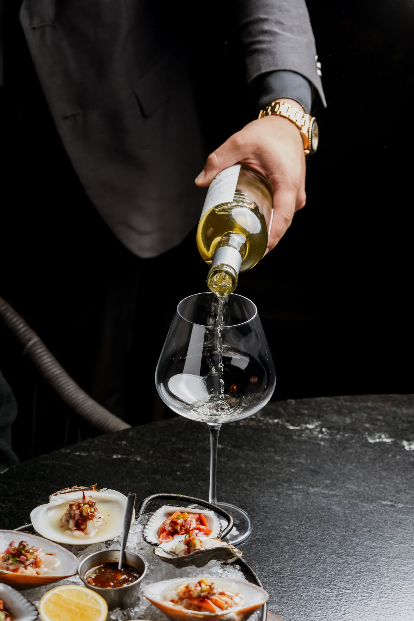 Mesero que sirve vino blanco en una copa junto a platos de entradas