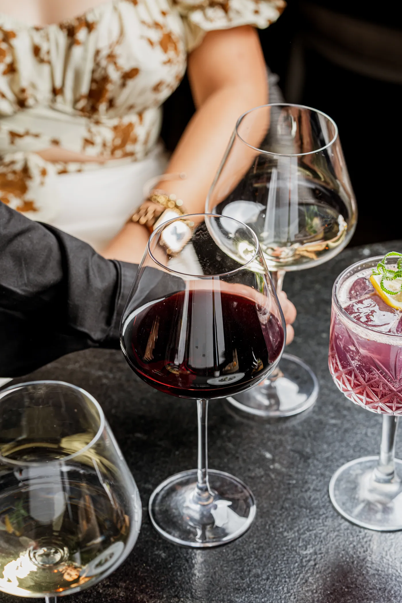 Copas de vino tinto y blanco y un coctel rosado en una mesa con comensales